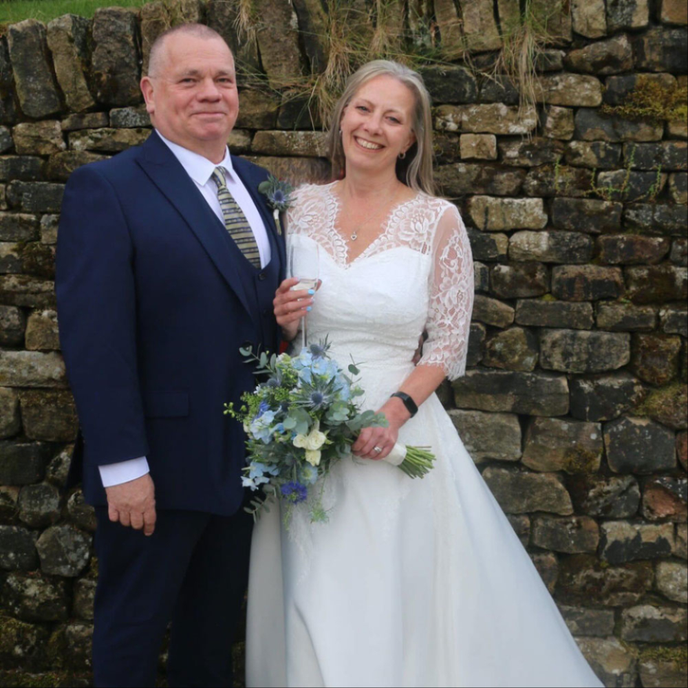 Newlywed couple with bridal bouquet by a stone wall