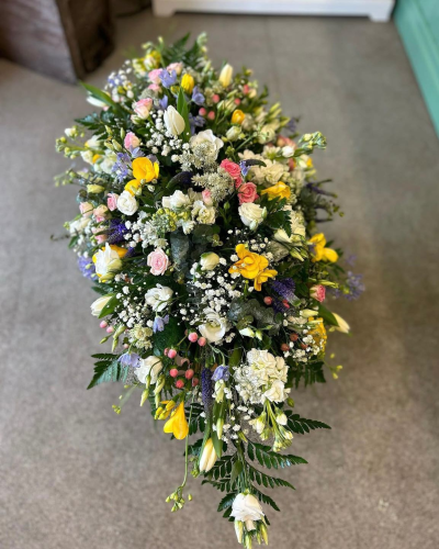 Meadow Grace Spray - A beautifully handcrafted spray featuring a delicate blend of soft pastel shades with touches of sunny yellow, fresh white and gentle lavender tones. Flowing naturally with elegant greenery and graceful textures, this tribute offers a peaceful and heartfelt expression of love, remembrance and comfort. A timeless choice for honouring a cherished life with warmth, beauty and dignity.