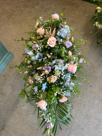 Pastel Garden Spray - A beautifully handcrafted tribute arrangement inspired by the gentle beauty of an English country garden. Designed in soft pastel shades of blush, lavender, ivory, and delicate blue, this elegant display is complemented by flowing greenery and natural textures to create a graceful and comforting tribute. Thoughtfully arranged to honour a loved one with warmth and serenity, it is a fitting choice for funeral services, memorials, or celebration of life ceremonies. Each tribute is individually created by our skilled florists using the freshest seasonal blooms and foliage, ensuring every arrangement is unique and made with the utmost care and respect.